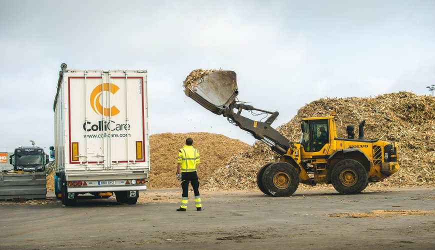 A branded ColliCare moving floor trailer being loaded with sawdust by a tractor