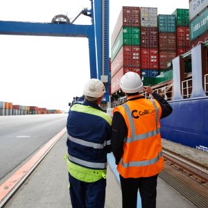 Two people at the dock making sure the loaded containers are ready to be shipped by sea.