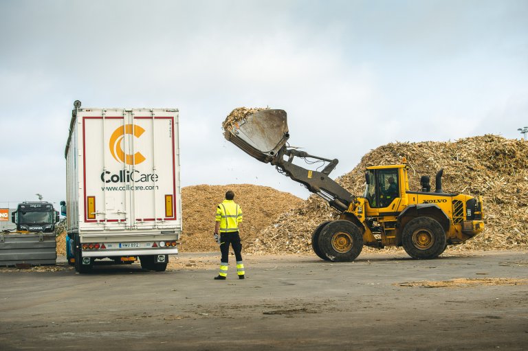 A branded ColliCare moving floor trailer being loaded with sawdust by a tractor